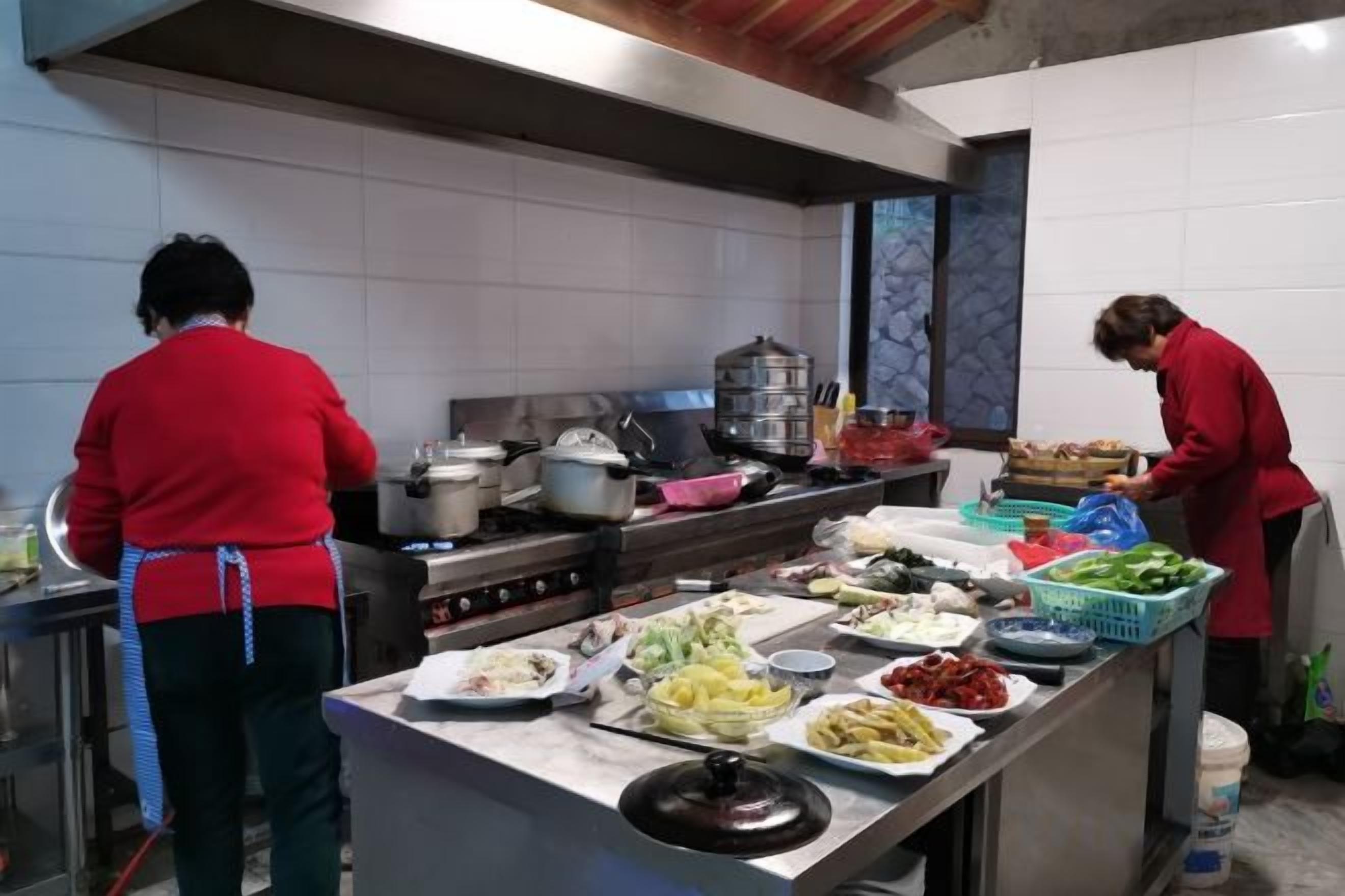 Een keuken met koks die eten bereiden, diverse gerechten in het zicht en kookapparatuur.