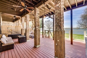 Terraza exterior cubierta con mobiliario de mimbre, piso de madera y vista a un cuerpo de agua.
