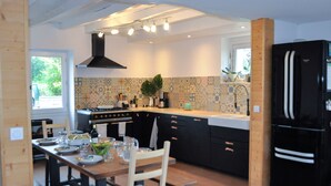 Una cucina moderna con zona pranzo, caratterizzata da un frigorifero nero, zoccolo in piastrelle e mobili in legno.
