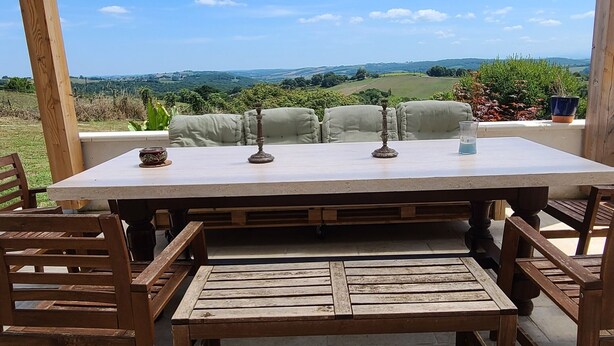 Un'area pranzo all'aperto riparata, con tavolo e panche, circondata da una pergola in legno, affacciata su un paesaggio suggestivo.