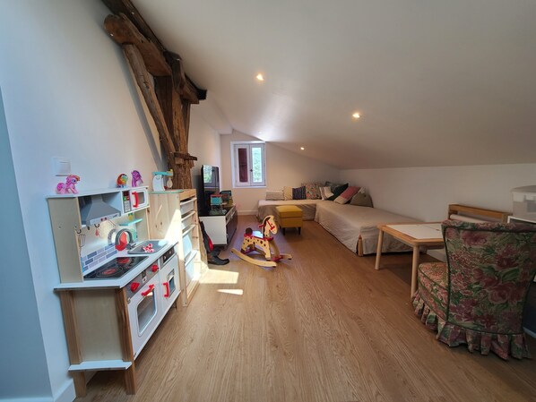 A cozy attic bedroom with a loft bed, a wooden play kitchen, and a rocking chair.