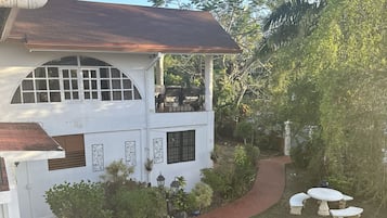 Une maison blanche avec un balcon, une terrasse dallée avec des meubles d’extérieur et un jardin.