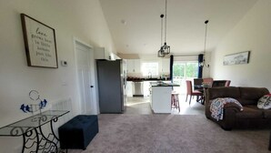 En rummelig opholdsstue med et køkken i baggrunden, et spiseområde med bord og stole, og en hyggelig siddeplads med en sofa.