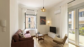 Un soggiorno moderno con un divano, una poltrona e un tavolino da caffè. C'è una TV su un mobile, un quadro al muro e una finestra con tende.