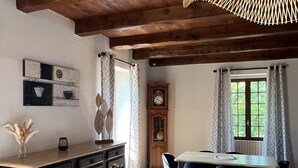 En matplats med ett träpanelat tak, ett matbord med stolar, en klocka och ett fönster med gardiner.
