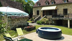 En trädgård med en bubbelpool, solstolar och en byggnad i sten med ett tak täckt av tegelpannor.