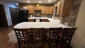 A kitchen with wooden cabinets, a large island, and four chairs. - Cozy Cabin, Less than 1/2 mile to Marina, Boat Trailer Parking (Theodosia)