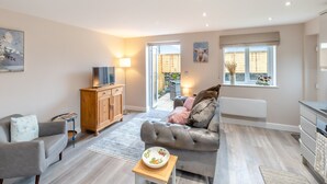 A spacious living room with a grey sofa, a wooden cabinet, and a television. - Oswald’s Rest is in an absolutely charming location and is perfect for couples. (Bamburgh, near Seahouses)