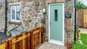 A stone building with a green door, a window, and a sign reading "Oswald's Rest". - Oswald’s Rest is in an absolutely charming location and is perfect for couples. (Bamburgh, near Seahouses)