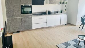 Una cocina moderna con armarios grises, horno empotrado y campana extractora negra. Hay encimeras blancas y una pequeña isla con un lavamanos.