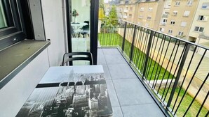 A balcony with a table featuring a cityscape print, a chair, and a view of neighboring apartment buildings. - New 1 bedroom in City Center- Terrace (Luxembourg City)