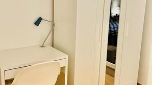 Una habitación con un escritorio blanco, una silla y un armario con espejo.