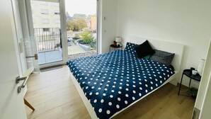 A bedroom with a bed, a nightstand, a lamp, and a view of the outside. - New 1 bedroom in City Center- Terrace (Luxembourg City)