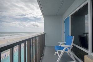 A balcony with a view of the beach and pool, a blue chair, and a TV.