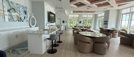 A modern kitchen with a central island, bar stools, and a dining area with round tables and chairs.