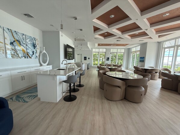 A modern kitchen with a central island, bar stools, and a dining area with round tables and chairs.