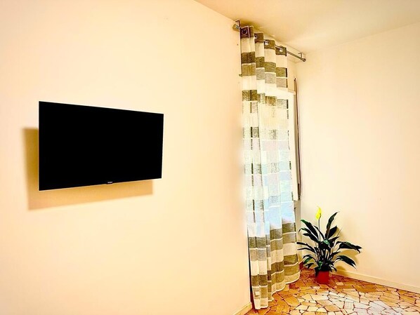 Habitación con televisor de pantalla plana montado, cortina de ducha estampada, planta en maceta y suelo de baldosas.