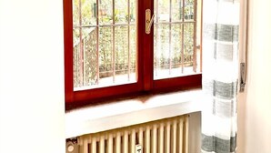 Une pièce avec une fenêtre ornée d’une grille métallique, un radiateur en dessous et un rideau à rayures sur le côté droit.