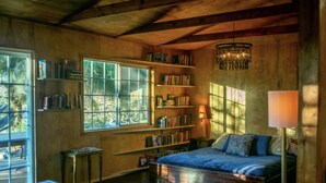 A cozy bedroom with a large bed, bookshelves, a chandelier, and a view through the window. - The Library at The Sea of Tranquility w/ Pool, Hot Tub & Outdoor Kitchen (Yucca Valley)