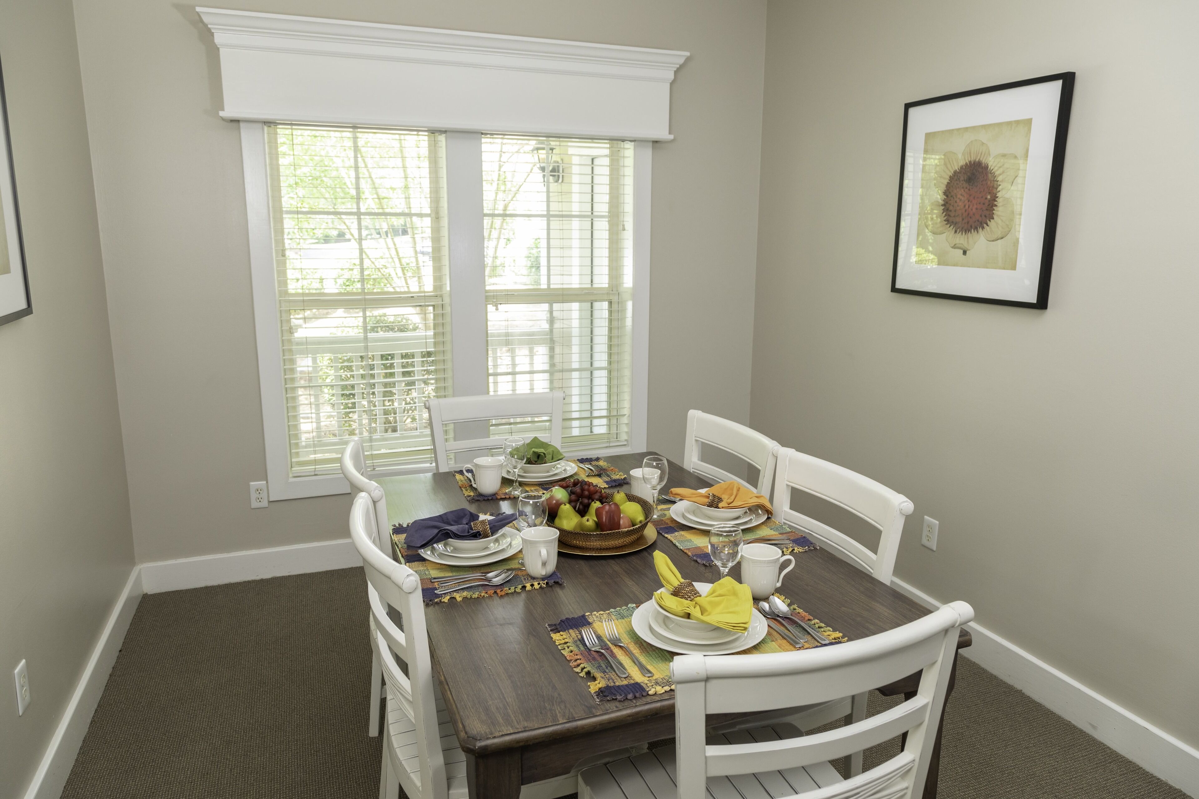 A dining room with a table set for four, including plates, cutlery, and a fruit bowl.