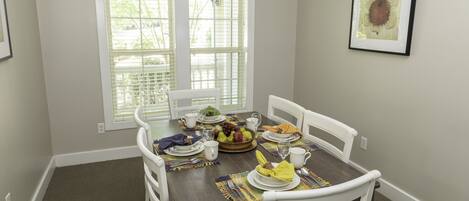 A dining room with a table set for four, including plates, cutlery, and a fruit bowl.