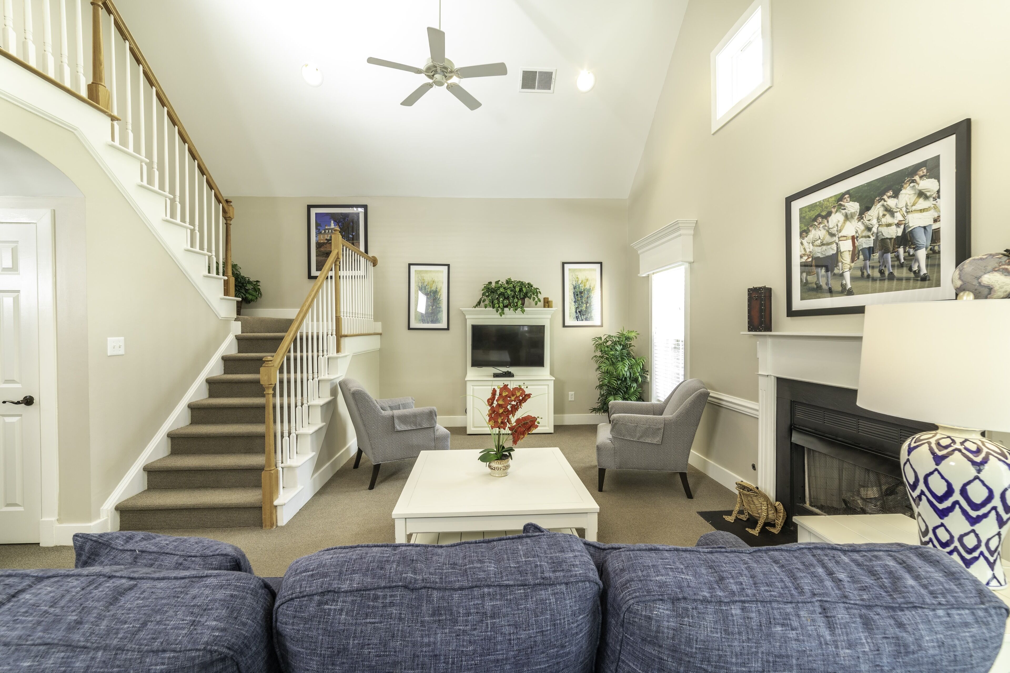 A living room with a staircase, a fireplace, a television, and a large framed picture on the wall.