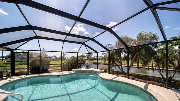 A covered swimming pool with a view of a lake and palm trees. - Southern Breeze - Spacious, canal view home (Rotonda West)
