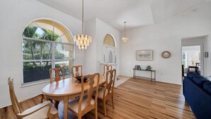 A dining area with a wooden table and chairs, large windows with blinds, and a chandelier. - Southern Breeze - Spacious, canal view home (Rotonda West)