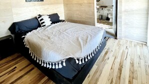 Ein Schlafzimmer mit Holzboden, einem Bett mit weiß-schwarzem Überwurf, einem schwarzen Kopfteil und einer Wandleuchte.