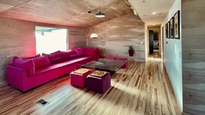 Ein modernes Wohnzimmer mit Holzbalkendecke, einem rosa Sofa und einem Glastisch.