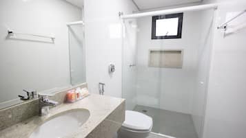 Un baño moderno con encimera de granito, un lavamanos blanco, ducha con mampara de vidrio y un inodoro.