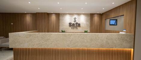 A reception area with a marble counter, wooden paneling, a sign for 'Safa Hotel', and a mounted television.