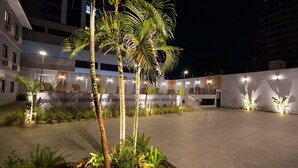 Un espace extérieur bien éclairé, agrémenté de palmiers, de chaises longues et doté d’une façade de bâtiment moderne.
