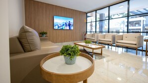 Un hall d’entrée moderne avec un canapé, des fauteuils, une table basse agrémentée d’une plante et un téléviseur fixé au mur.