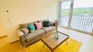 A living room with a sofa, a coffee table, and a large window. - Luxury 2023 Flat in city center. Parking (Luxembourg City)
