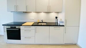 A compact kitchen with white cabinets, a black countertop, and a built-in oven. - Luxury 2023 Flat in city center. Parking (Luxembourg City)