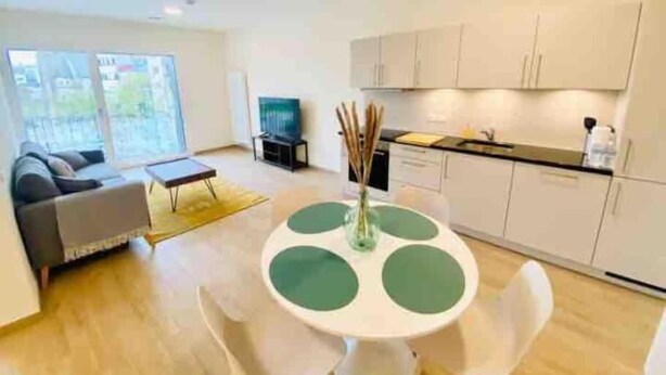 A modern living room with a sofa, a coffee table, and a dining table with chairs. There is a kitchen area with cabinets and a countertop. - Luxury 2023 Flat in city center. Parking (Luxembourg City)