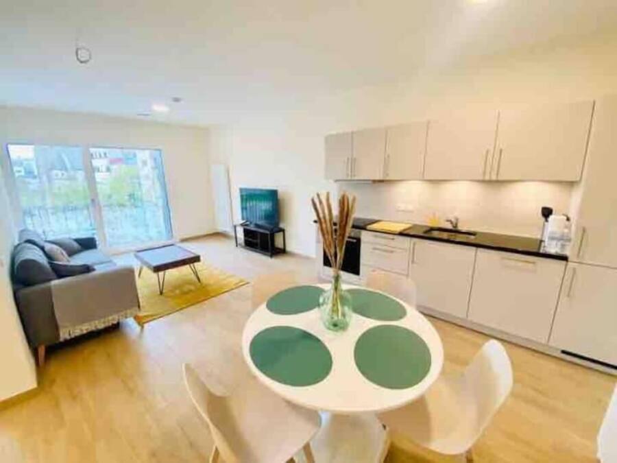 Un salon moderne comprenant un canapé, une table basse et une table à manger avec des chaises. Il y a également un coin cuisine avec des placards et un plan de travail.