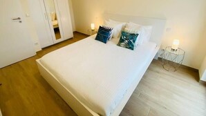 A bedroom with a large bed, white walls, and a wooden floor. There is a wardrobe with a mirror and a door. - Luxury 2023 Flat in city center. Parking (Luxembourg City)