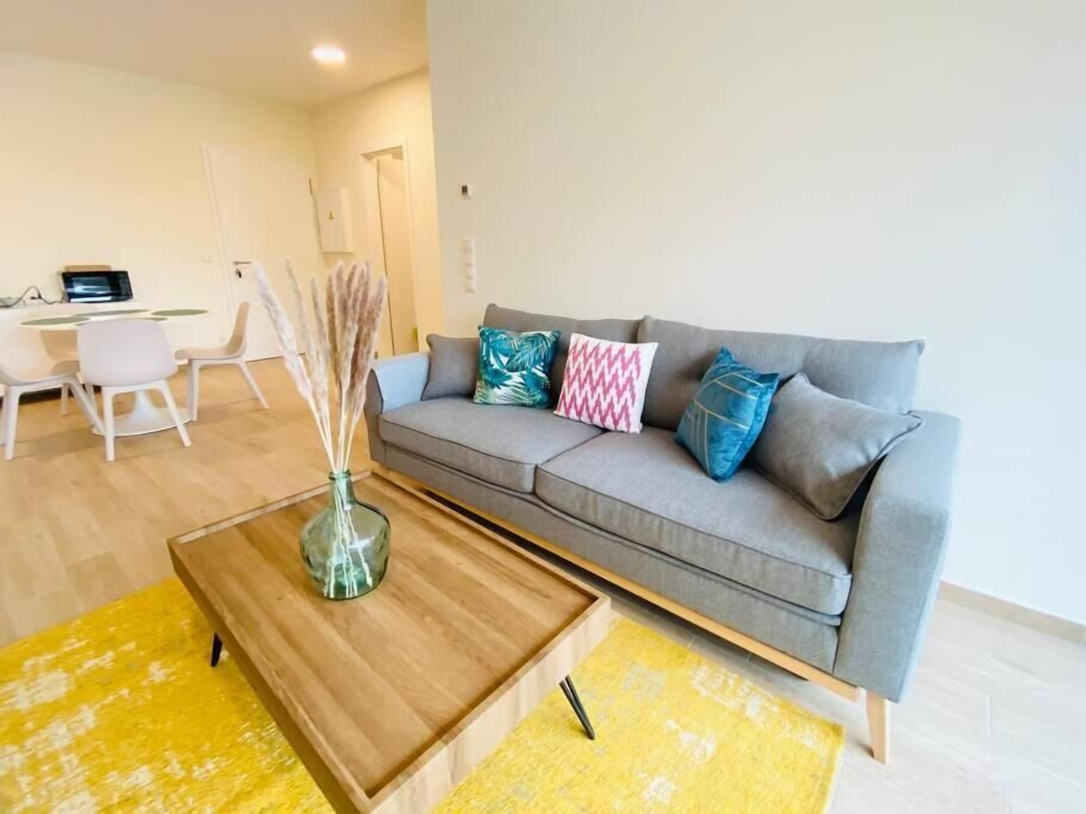 Un salon moderne avec un canapé gris, des coussins colorés, une table basse en bois et un tapis jaune.