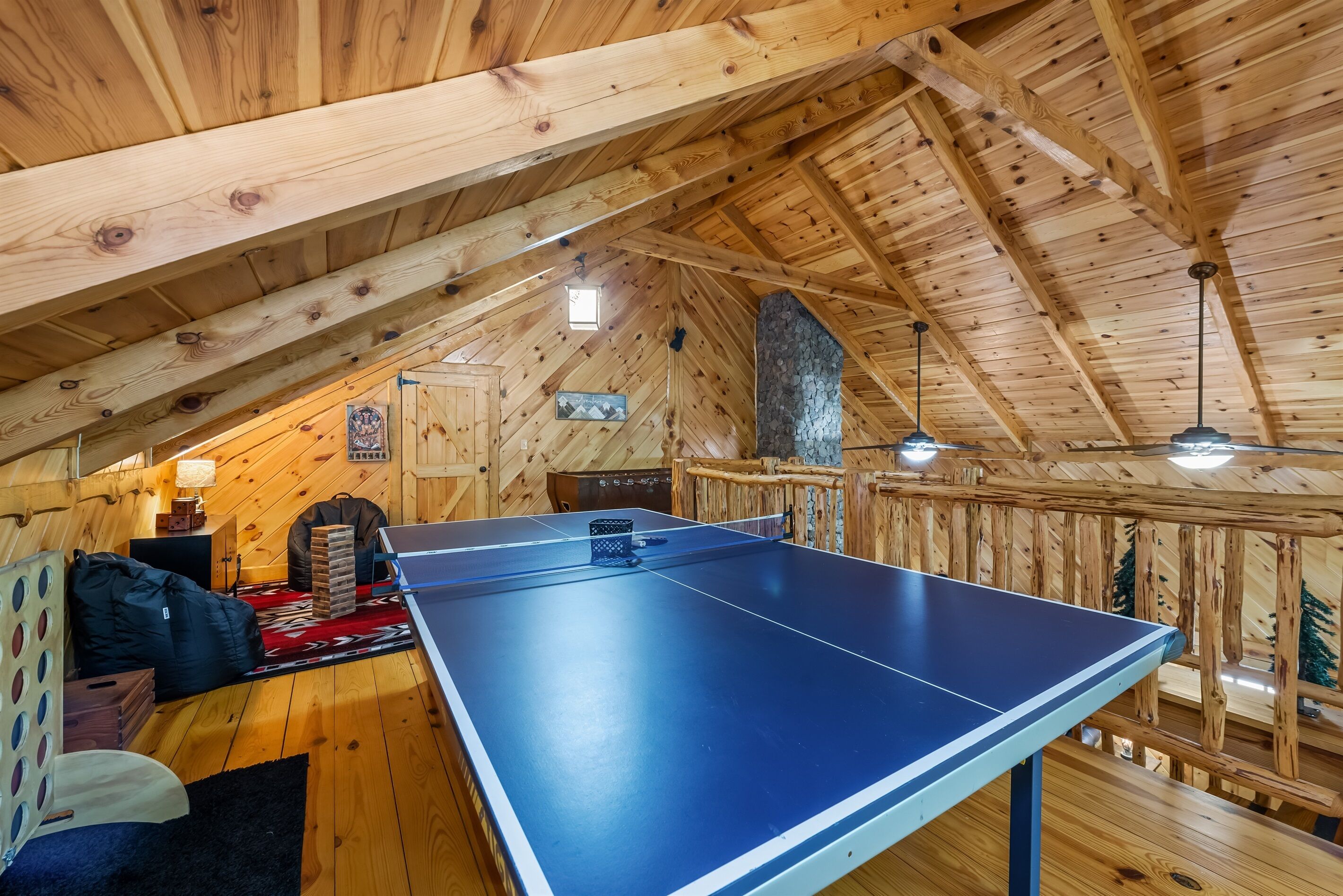 A ping pong table in a wooden room with a sloped ceiling and a stone wall.