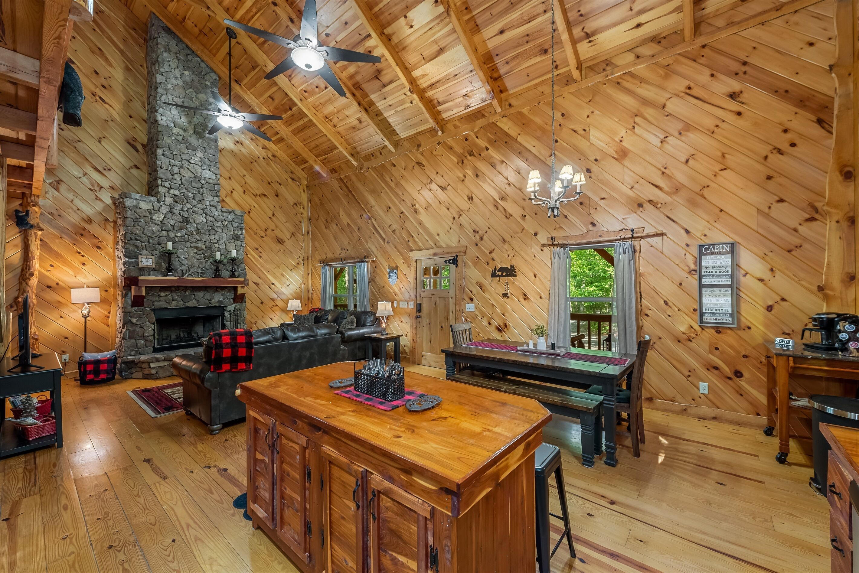 A cabin interior with a stone fireplace, wooden ceiling, and a dining area.