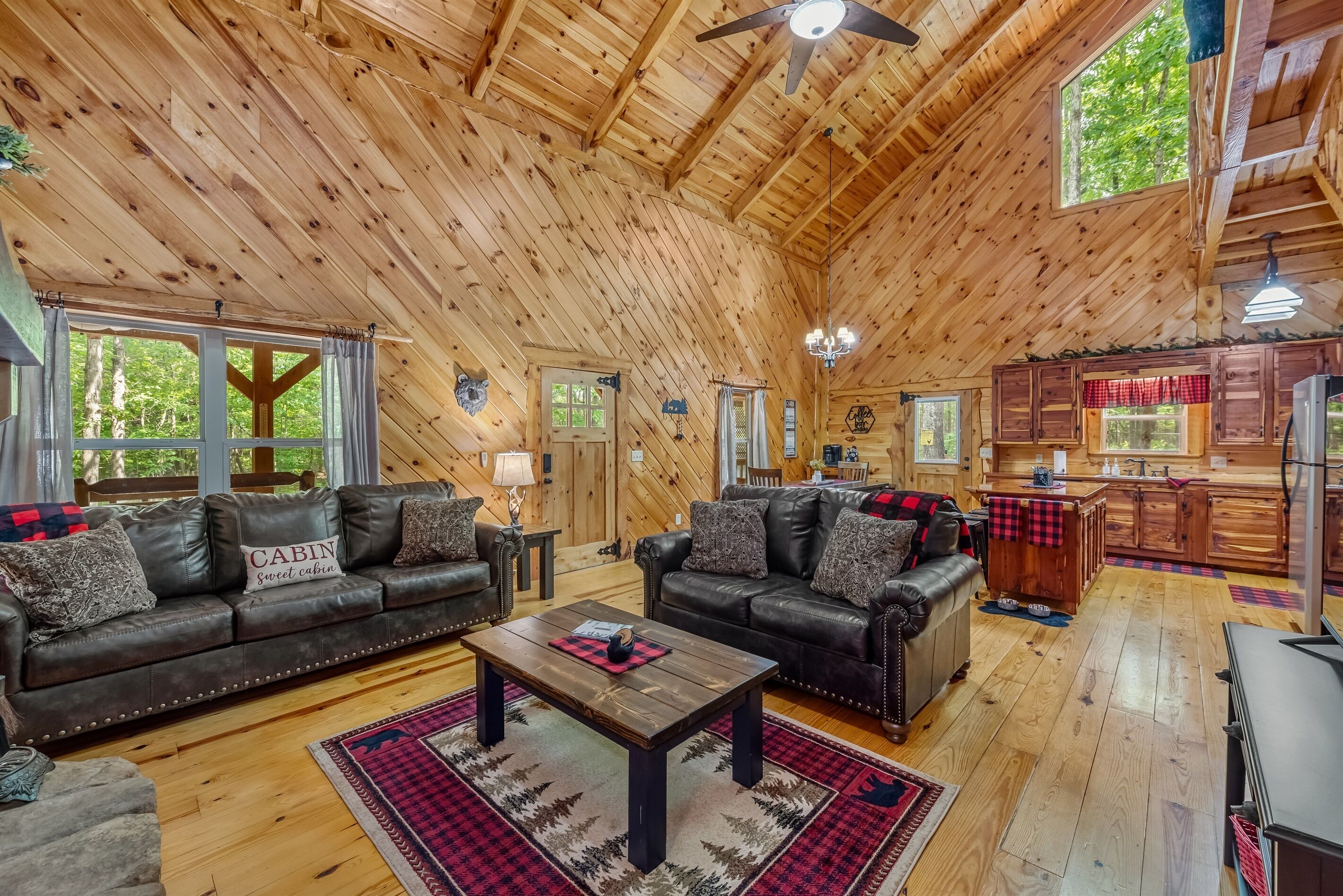 A spacious cabin interior with two leather sofas, a wooden coffee table, and a kitchen area.