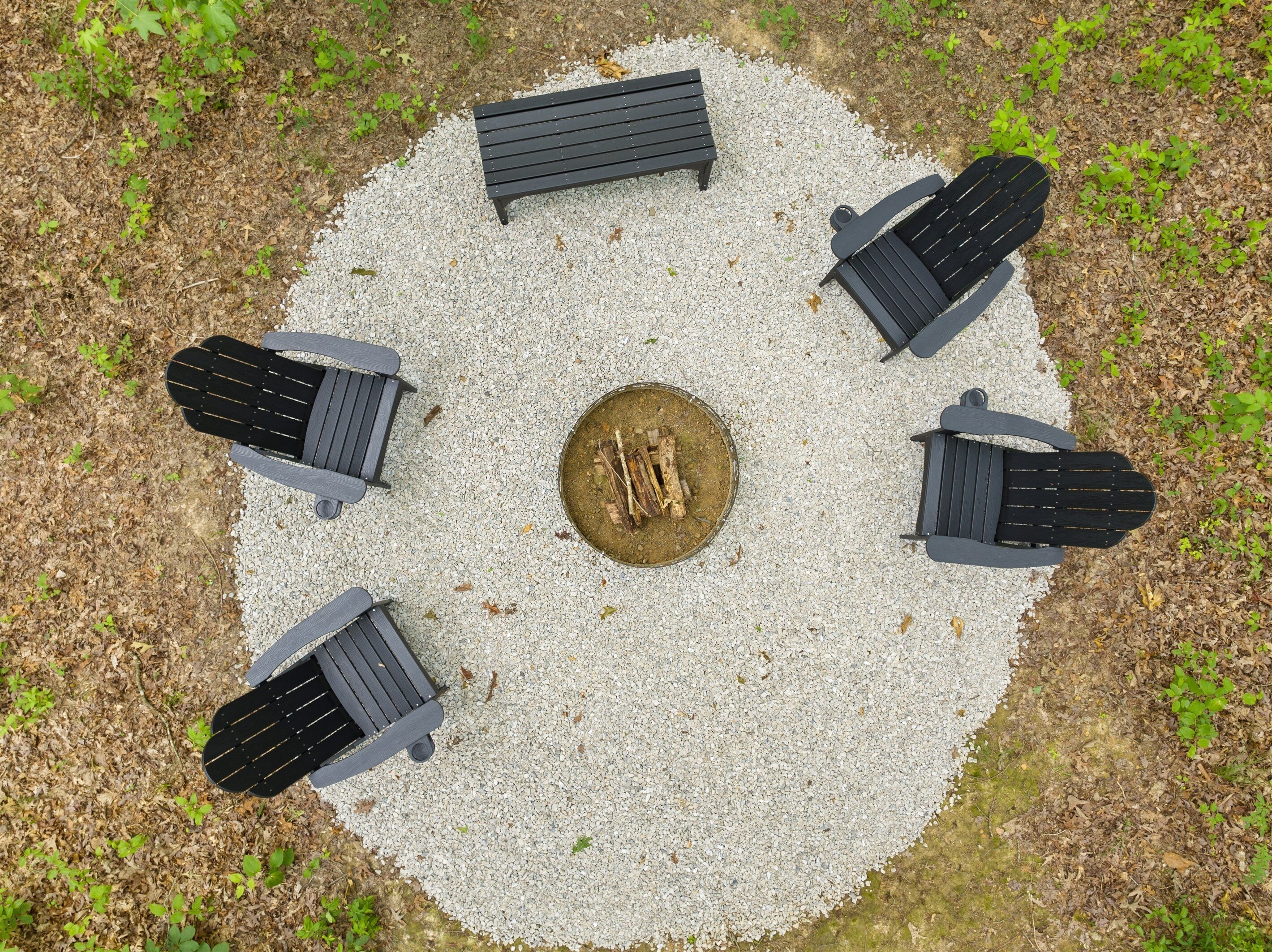 A circular outdoor seating area with six black benches arranged around a central fire pit.