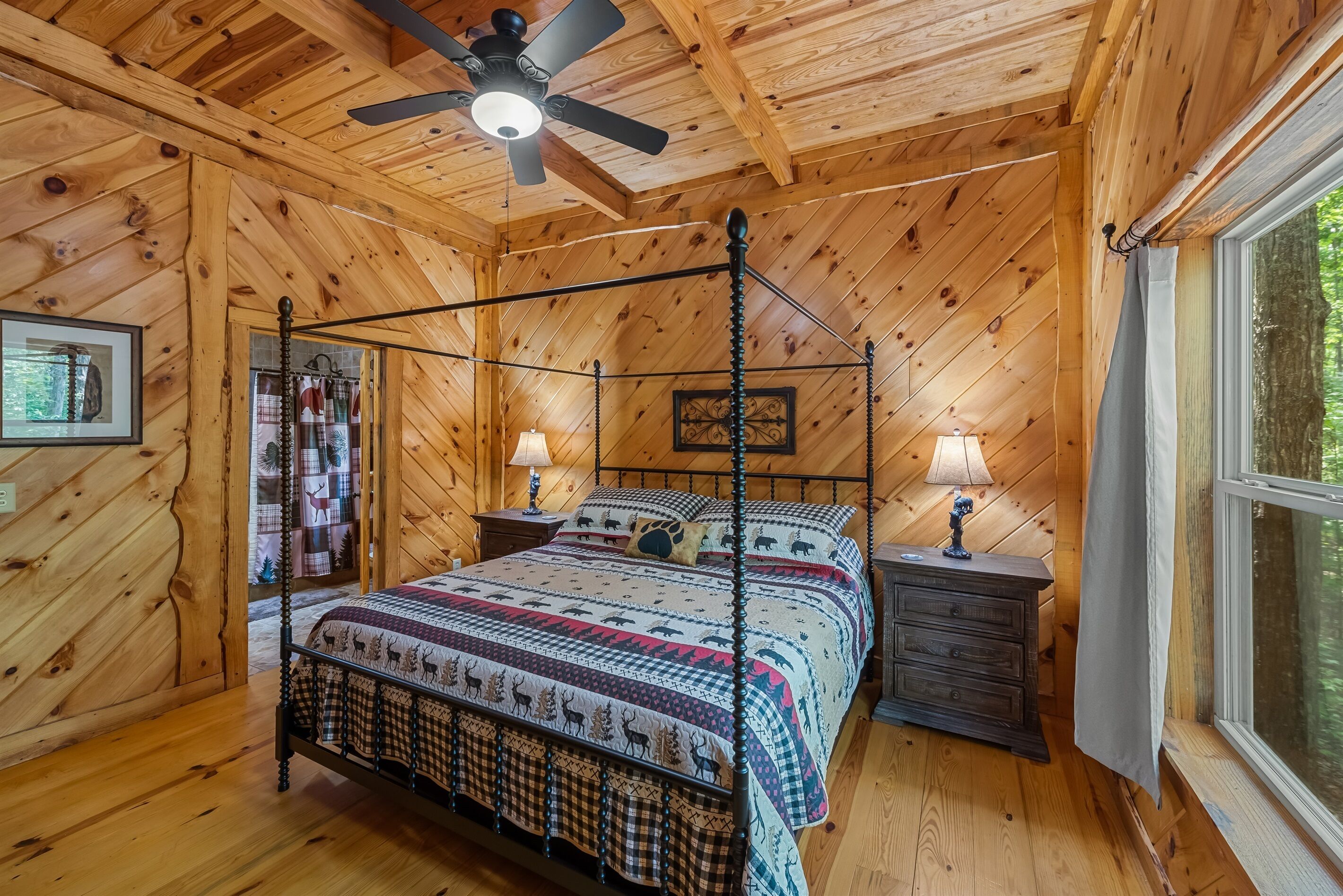 A wooden cabin bedroom with a four-poster bed, two bedside tables, a ceiling fan, and a window with curtains.