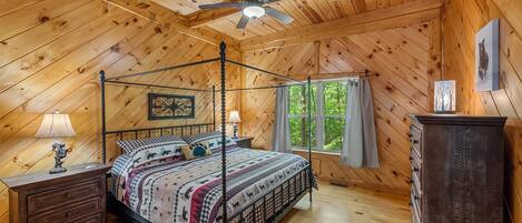Een slaapkamer in een houten chalet met een hemelbed, een plafondventilator, een kapstok en een raam met gordijnen.