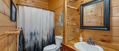 Une salle de bain rustique, aménagée dans une cabane en bois, comprenant des toilettes, un rideau de douche, un lavabo et un miroir.