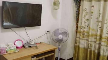 Una habitación con una televisión instalada en la pared, un escritorio con un ventilador y una cortina de diseño tradicional.
