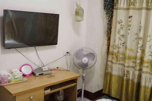 Una stanza con televisore a parete, una scrivania con ventilatore e una tenda dal disegno tradizionale.