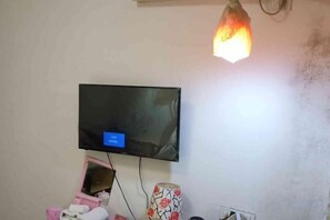 Una stanza con una televisione a parete, un mobile contenitore rosa e una lampada decorata.